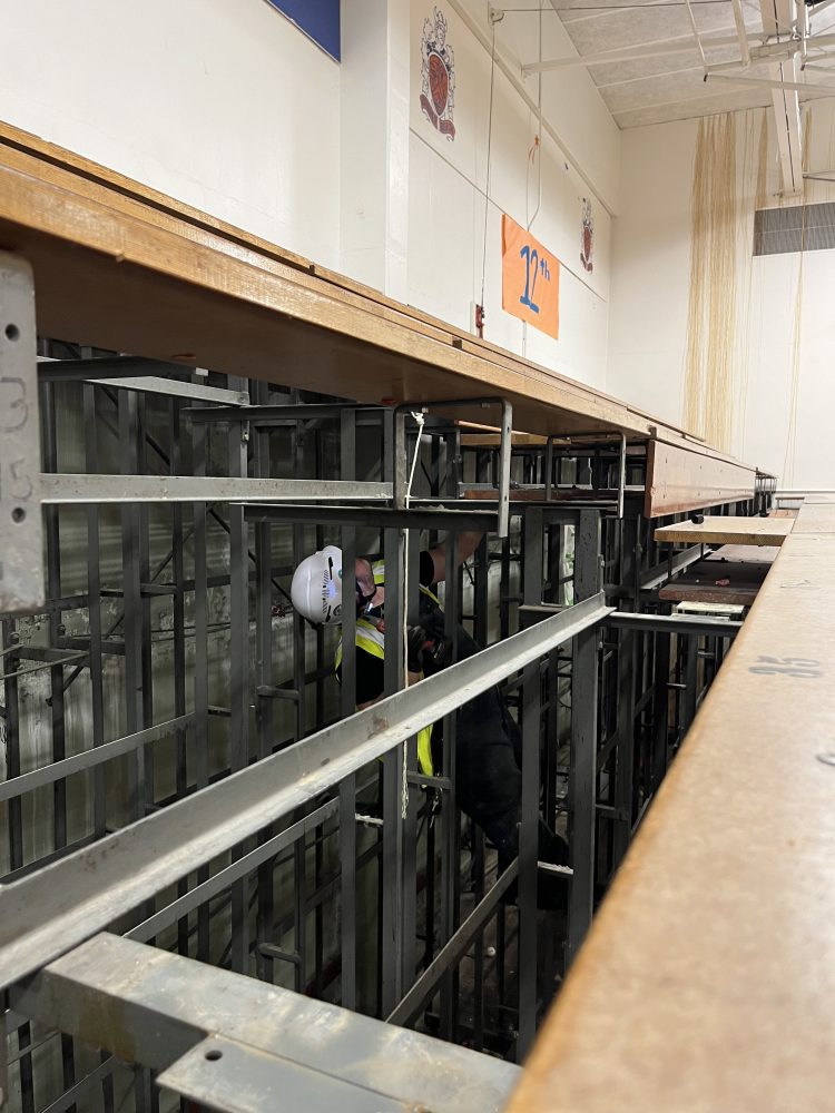 Person removing the bleacher boards while climbing in the metal structure